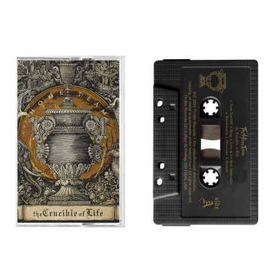 A black cassette from The Home Team with a metallic gold imprint, a transparent window, and housed in a clear Norelco box featuring ornate urn artwork, foliage, and the text “the Crucible of Life.”.