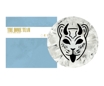 A limited edition 12” jacket by The Home Team holds an opaque white vinyl with a black and white abstract animal face, beside a blue cover labeled “The Home Team Live at Abbey Road” in yellow and white text.